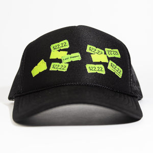 A black trucker-style cap with neon yellow-green embroidered price tags on the front, photographed against a plain white background.