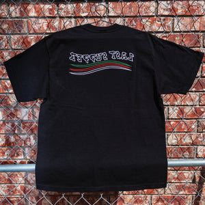 Black t-shirt with a logo on the back against a brick wall.