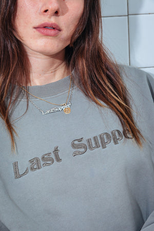 Person wearing a gray sweatshirt with 'Last Supper' text, close-up of face and upper body.